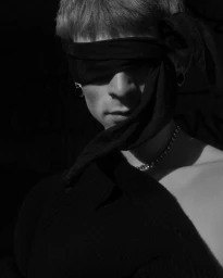 Close-up black and white portrait of a person wearing a dark blindfold and a chain necklace, captured by Daniil Kudryavtsev.