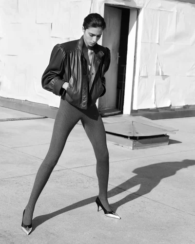 Model wearing a dark leather jacket and textured tights posing outdoors on a rooftop in black and white.