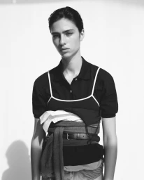 Model with slicked-back dark hair wearing layered black and white clothing against a plain background