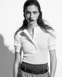 A woman wearing a white ribbed polo shirt and a dark belt against a plain white background