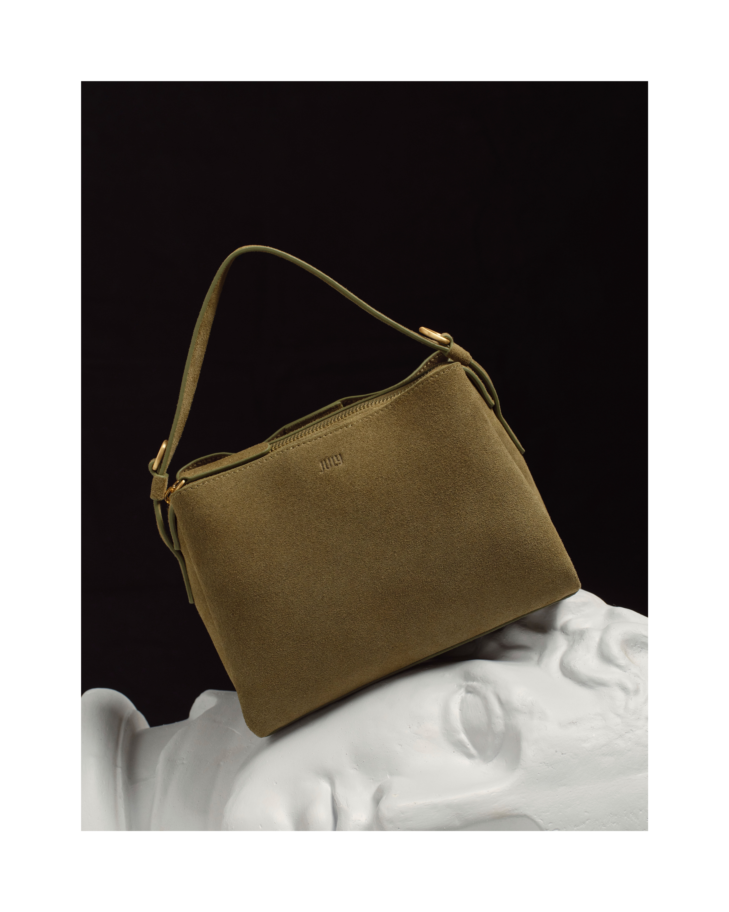 Olive-green suede shoulder bag on a white bust against a dark background. Fashion, design, product photography, accessory.