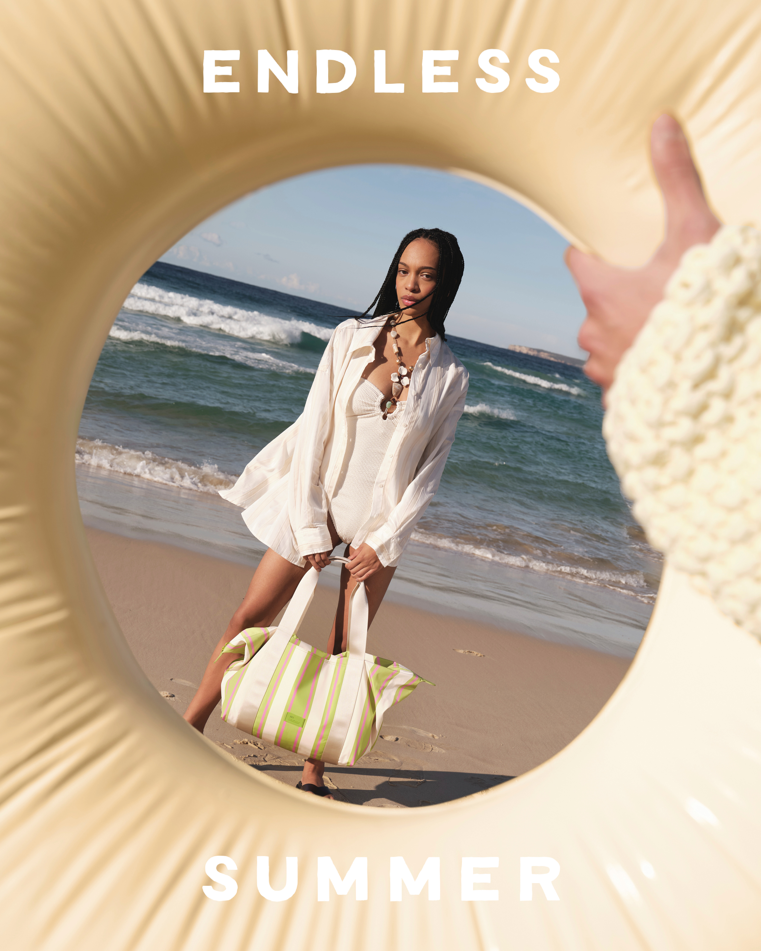 A woman in light clothing stands on a beach with a striped bag, framed by a yellow inflatable ring, with the ocean in the background.