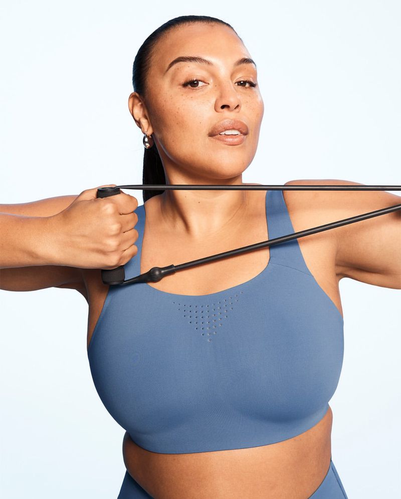 Athletic woman in blue sports bra uses resistance band for upper body workout against a clean, bright background in a medium studio shot.