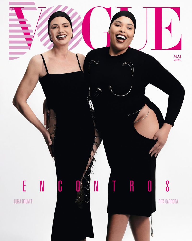 Two women pose on a Vogue cover, one wearing a black strappy dress and the other a long-sleeved dress with silver embellishments.