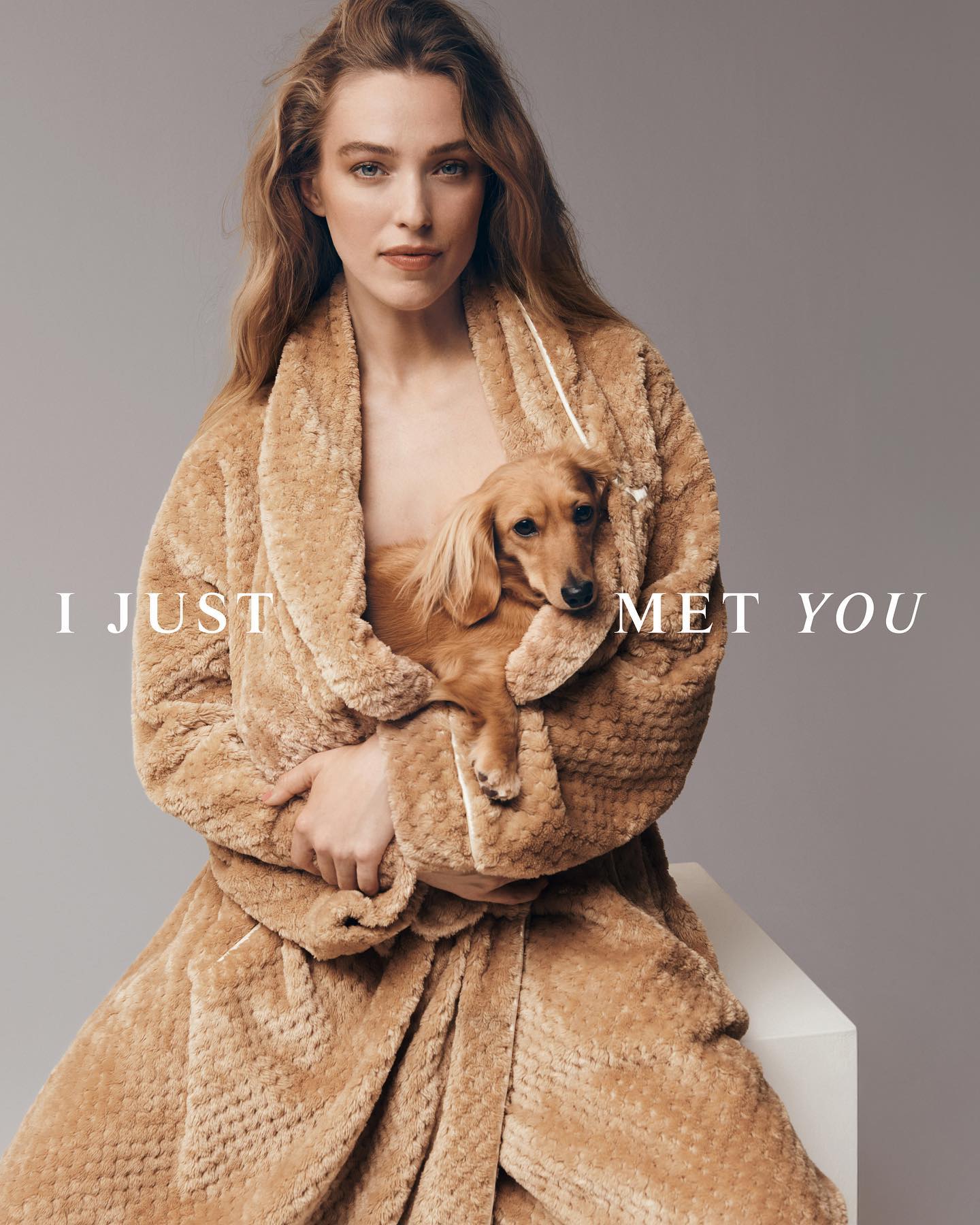 Attractive woman in robe sits while holding a tan dachshund dog in her arms in an eye-level shot in an indoor setting.
