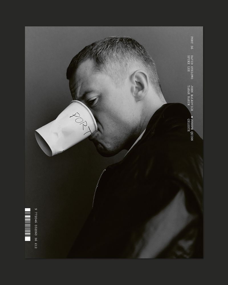 Black and white studio portrait of a man with short hair drinking from a white paper cup with the handwritten word 'PORT' on it.
