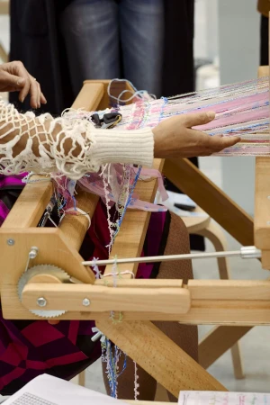 Close-up of a person weaving with a wooden loom, showcasing hands manipulating colorful threads, creating an artisanal textile.