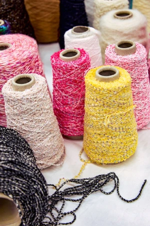 Colorful collection of yarn spools in yellow, pink, white, and black, creating a textured and vibrant display on a white surface.