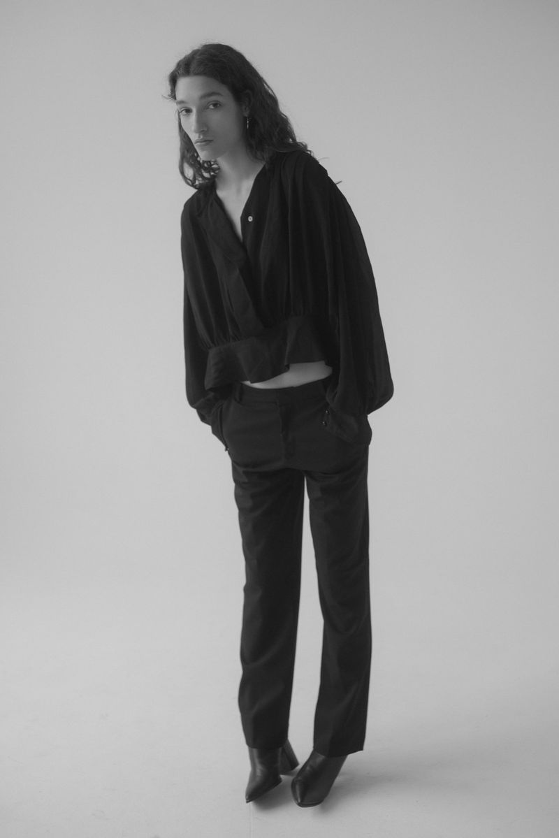 Monochrome fashion shot of a slender adult female model with long wavy hair wearing a black wrap top and pants in a photo studio.