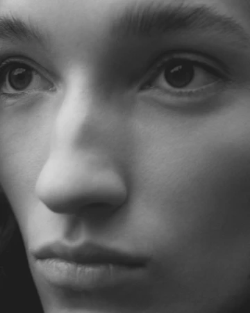 Close-up black and white portrait of a person featuring detailed eyes, nose, and lips under soft lighting, highlighting facial features.