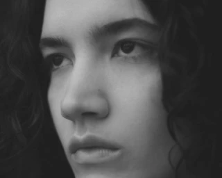 Close up monochrome portrait of a young person with dark curly hair looking away