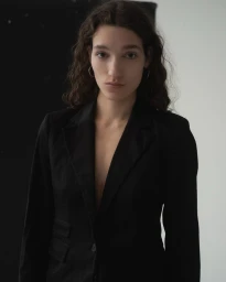 Portrait of a woman with dark wavy hair wearing a black blazer against a split black and white background.