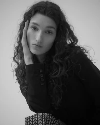 Portrait of a woman with long curly hair touching her face against a plain background