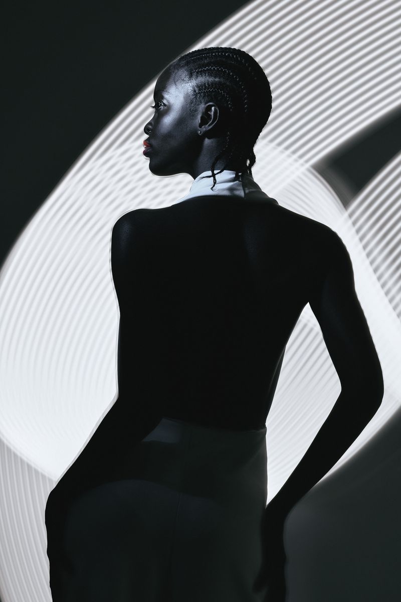 Striking profile shot of an African-American woman with braided hair looking left, illuminated by linear white light patterns.