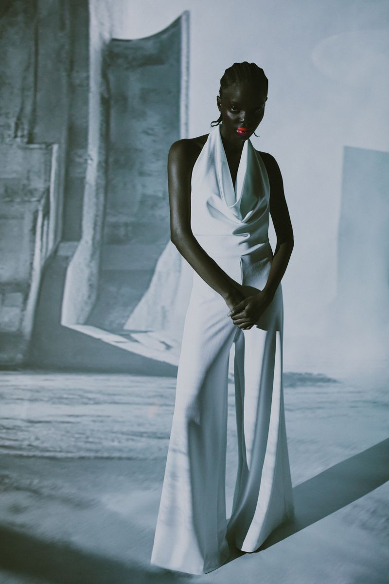 Elegant woman in a white jumpsuit posing against an abstract architectural backdrop, creating a striking fashion editorial image.