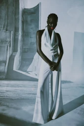Black woman wearing a white halter jumpsuit with bright pink lipstick against a textured background in a portrait by Jeanne Dart.