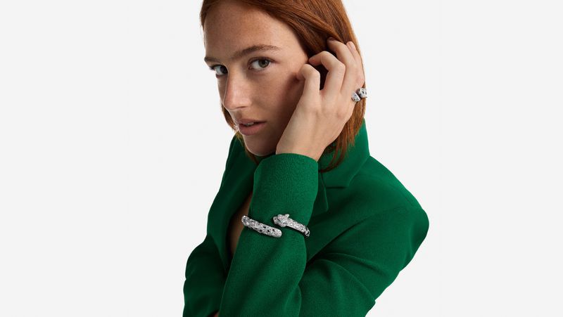 Portrait of a red-haired model in a green jacket, showcasing a jaguar ring and bracelet against a clean white background.