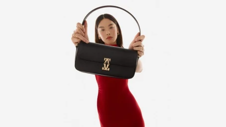 Model holding a black leather Cartier handbag with gold hardware against a clean white background