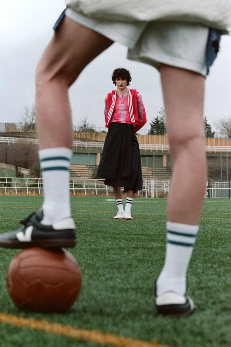 Two people in athletic wear on a green field, one with foot on soccer ball, showcasing contemporary sports fashion and outdoor style.