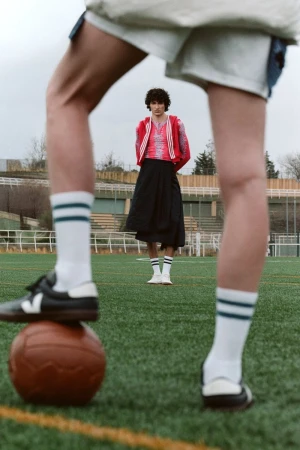 Two people in athletic wear on a green field, one with foot on soccer ball, showcasing contemporary sports fashion and outdoor style.