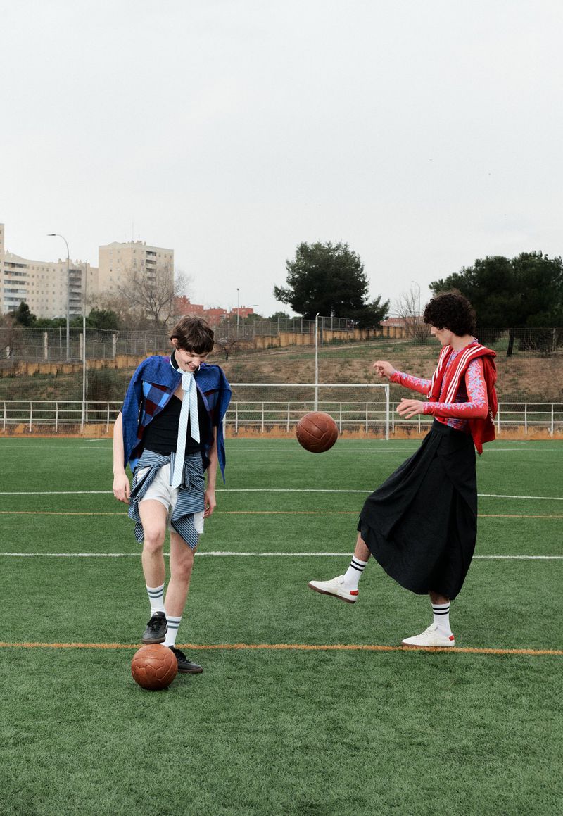 Two people playing soccer on a green field in daytime. Woman kicks ball in the air while another woman stands with a soccer ball at her feet.
