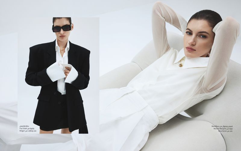 Fashion editorial shot of a brunette adult woman in an oversized black suit jacket and another woman in a white blouse and shorts.