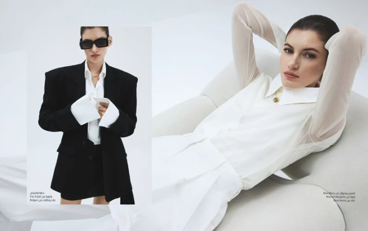 Fashion editorial shot of a brunette adult woman in an oversized black suit jacket and another woman in a white blouse and shorts.