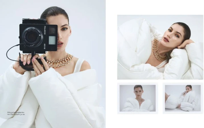 Woman in white jacket holds Polaroid camera with gold necklace against a plain white background in a fashion editorial layout.