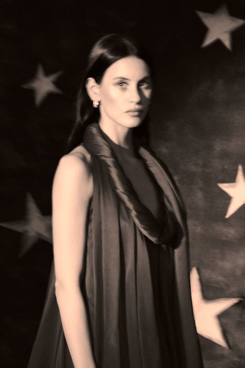 Elegant portrait of a woman with dark hair wearing a flowing shawl, set against a dark backdrop adorned with star patterns.