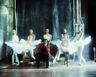Sampha sitting on a vintage settee surrounded by female ballet dancers in white tutus for To Be Magazine by Hector Clark