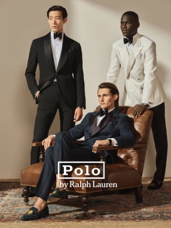 Three men in formalwear pose indoors on and around a leather chair. One man sits, one stands to the left, one leans on chair back.