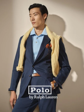 Asian man in a blue suit and light blue polo shirt with a yellow sweater draped around his shoulders posing in a studio.