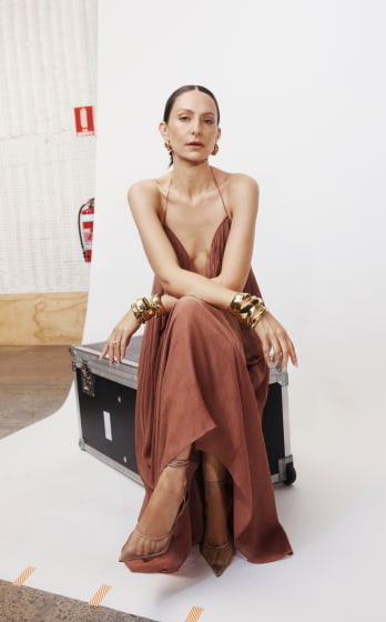 Elegant woman with golden bracelets posing in long dress. Woman seated on trunk in studio setting with soft lighting. Fashion shoot.