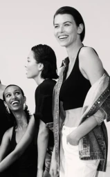 Three smiling female models posing together against a bright white seamless background in a monochrome fashion portrait.