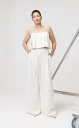 Model wearing a white pleated crop top and matching wide-leg trousers against a seamless white studio background.