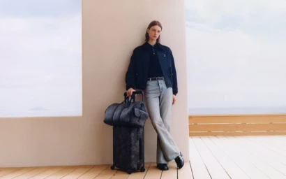 Model leaning against a wall on a wooden deck next to stacked luggage for Louis Vuitton pre-fall mens editorial