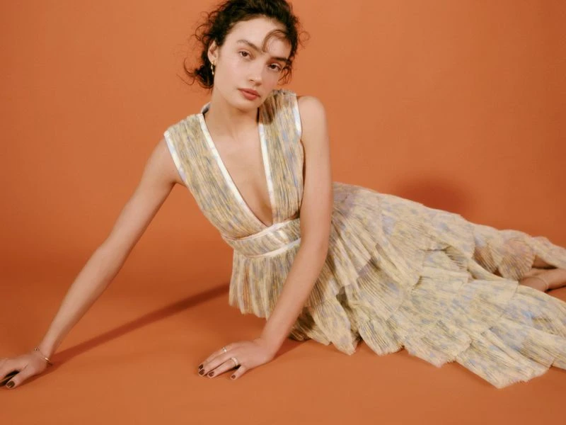 A woman lies in a light yellow dress with blue stripes on an orange background, posing for a fashion shot.