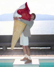 Man holding giant oversized ice cream cone sculpture by a pool for Christian Louboutin Fall 25 advertising campaign