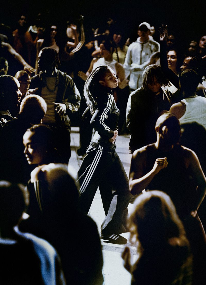 Adult female in black and white track suit with a crowd in the background. The scene is dark and illuminated from above.