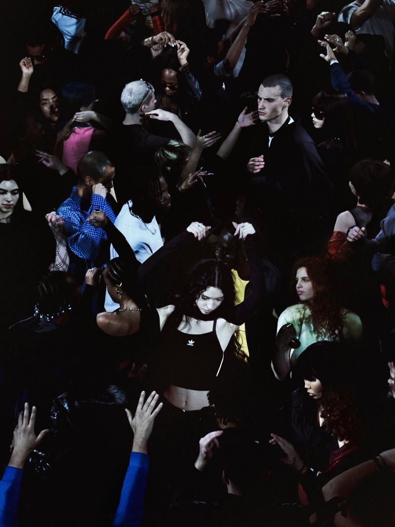 Diverse group of young adults dancing in a dark club setting. People are raising hands and moving to music, creating a vibrant atmosphere.