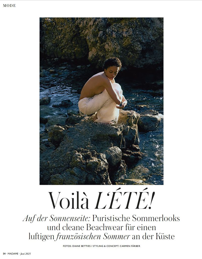 Woman in white knit pants sits on coastal rocks at the edge of the ocean, styled for a fashion editorial with natural light and textures.