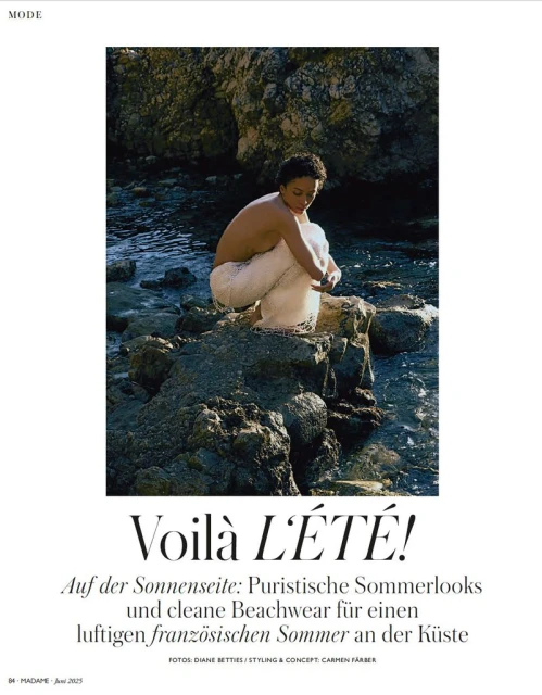 Woman in white knit pants sits on coastal rocks at the edge of the ocean, styled for a fashion editorial with natural light and textures.