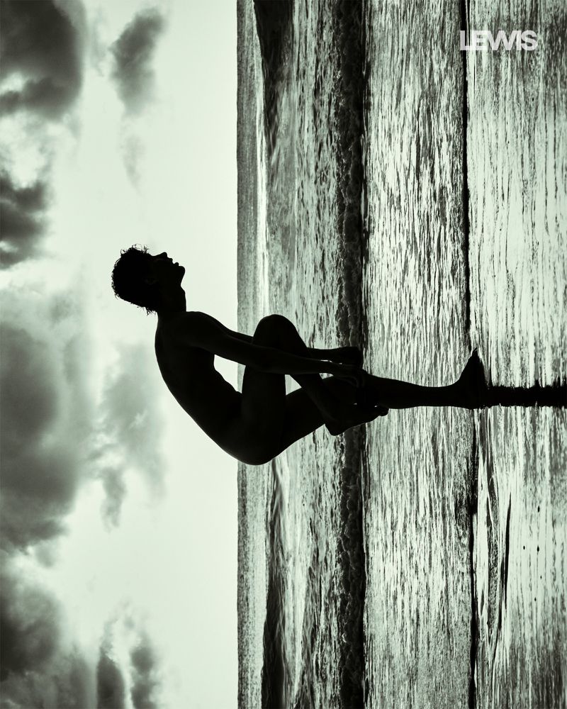 Monochrome silhouette of a person sitting against a backdrop of water meeting the sky, next to textured vertical patterns.