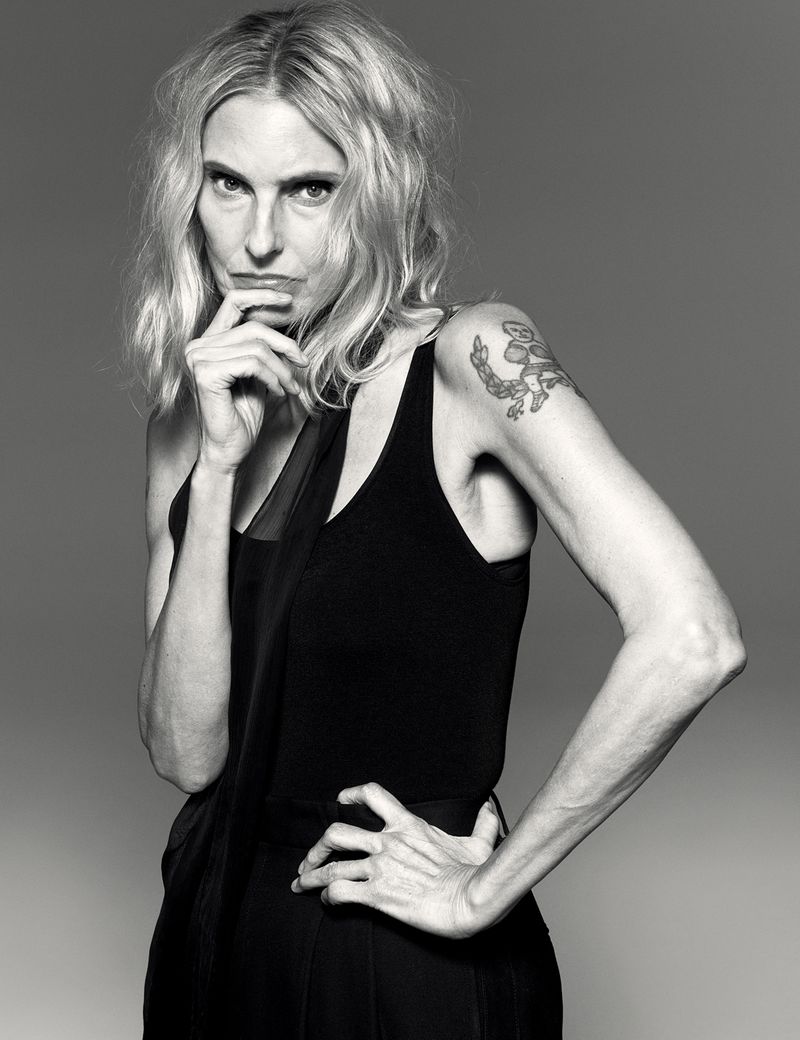 Striking black-and-white portrait of a blonde woman in a dark tank top, striking a pose with hand on her hip and pensive expression.