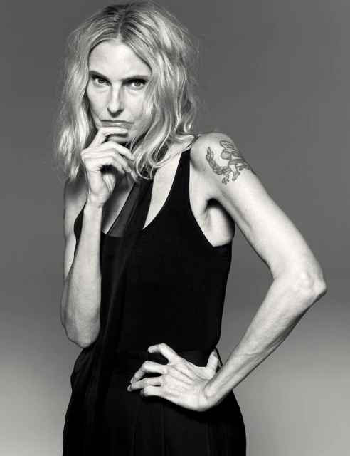 Striking black-and-white portrait of a blonde woman in a dark tank top, striking a pose with hand on her hip and pensive expression.