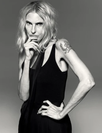 Striking black-and-white portrait of a blonde woman in a dark tank top, striking a pose with hand on her hip and pensive expression.