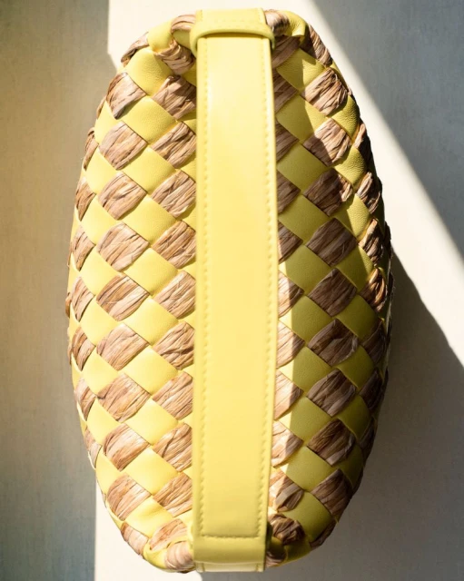 Close-up of woven handbag in yellow leather and natural raffia material with yellow leather handle, lit by bright sunlight.