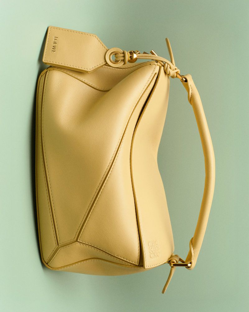 Luxury leather handbag by Loewe in yellow. Fashionable handbag with handle and detachable tag in studio environment on light green background.