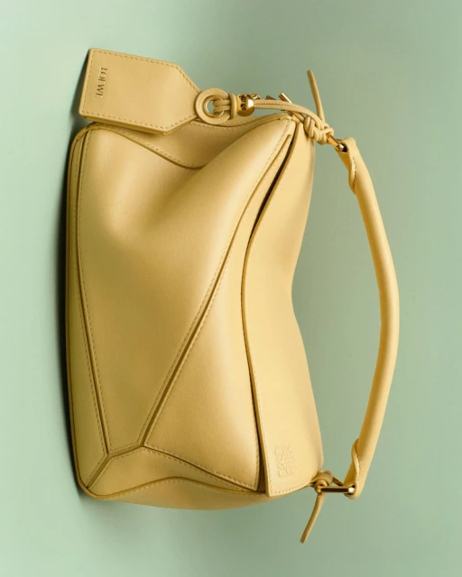Luxury leather handbag by Loewe in yellow. Fashionable handbag with handle and detachable tag in studio environment on light green background.