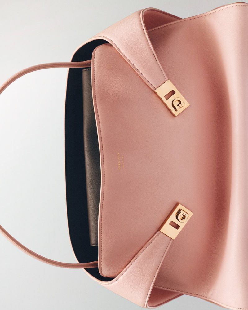 Pale pink Aigner tote bag with gold hardware and a black interior, photographed in portrait format with a high angle on a white backdrop.